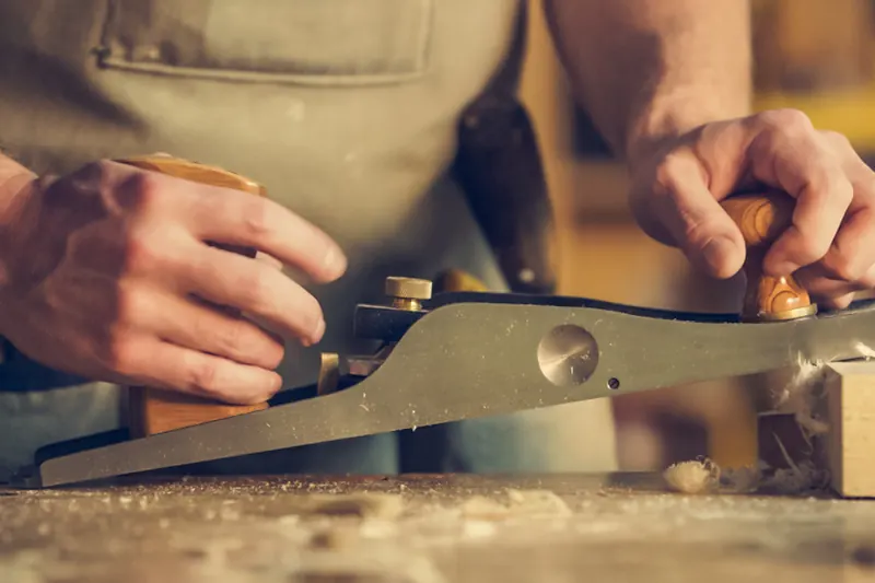 Mains d'un artisan travaillant le bois au rabot